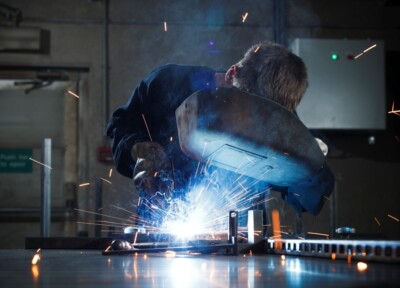 Welder performing metal fabrication with bright arc light and sparks in industrial workshop