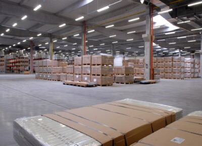 Large warehouse interior with palletized cardboard boxes and shelving racks under bright LED lighting
