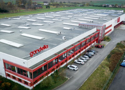 Gondella manufacturing facility with red and white warehouse building, flat roof with skylights, and parking area