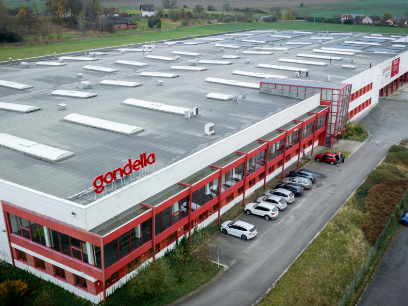 Gondella manufacturing facility with red and white warehouse building, flat roof with skylights, and parking area