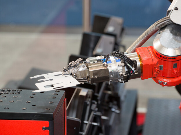 Robotic arm with gripper handling retail shelf component on assembly workstation