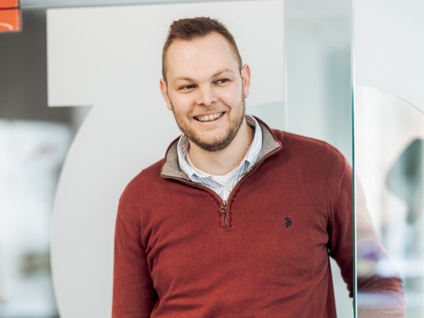 Chesney smiling in Gondella office wearing burgundy quarter-zip sweater