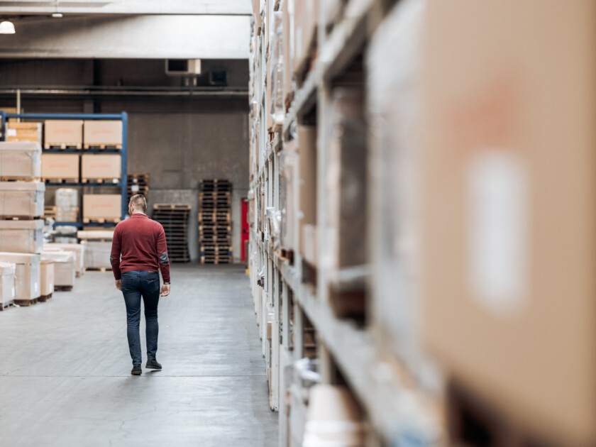 Worker walking through warehouse aisle lined with cardboard boxes and industrial shelving storage