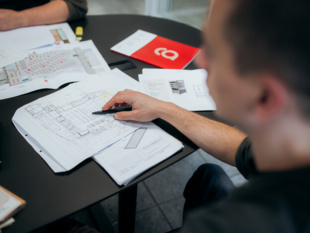 Design team reviewing retail shelving layouts and specifications at table with architectural blueprints and product samples