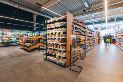 Delhaize supermarket aisle with Gondella shelving displaying packaged food products and snacks under modern lighting