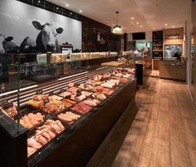 Modern butcher shop display with refrigerated meat counter, black tile walls, and cow photography mural