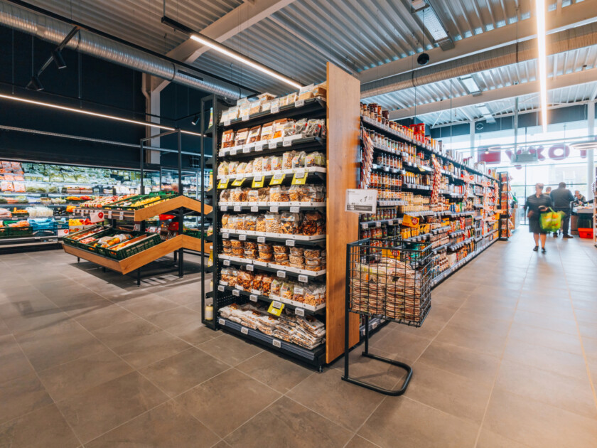 Delhaize supermarket aisle with Gondella shelving displaying packaged food products and snacks under modern lighting
