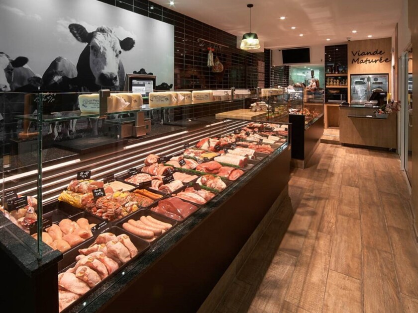 Modern butcher shop display with refrigerated meat counter, black tile walls, and cow photography mural