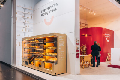 Gondola bakery display with illuminated shelving and warm wood finish, showcasing tailor-made bread furniture at Euroshop 2023