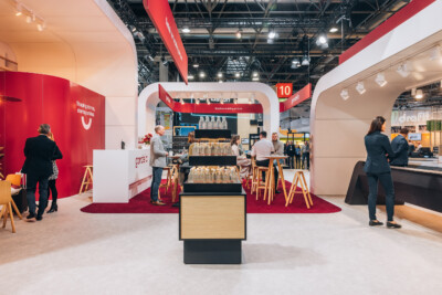 Gondella retail booth at Euroshop 2023 featuring red and white modular shopfitting display with wooden bar seating and product shelving