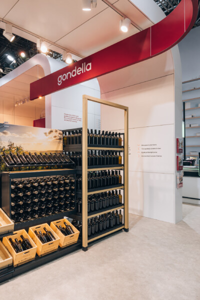 Gondella retail display booth at Euroshop 2023 featuring Pitch shelving with dark bottles, wooden display fixtures, and product samples in yellow crates