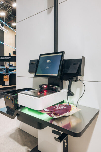 Axi self-checkout kiosk with touchscreen display and scanning platform at Euroshop 2023 retail technology exhibition