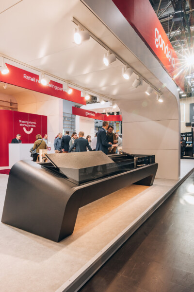 Gondella custom checkout counter with curved black design displayed at Euroshop 2023 trade show, visitors in background near red branded booth