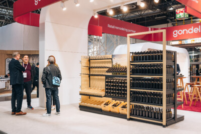 Gondel retail shelving display with wine bottles at Euroshop 2023, featuring wooden frame with black shelves and product samples