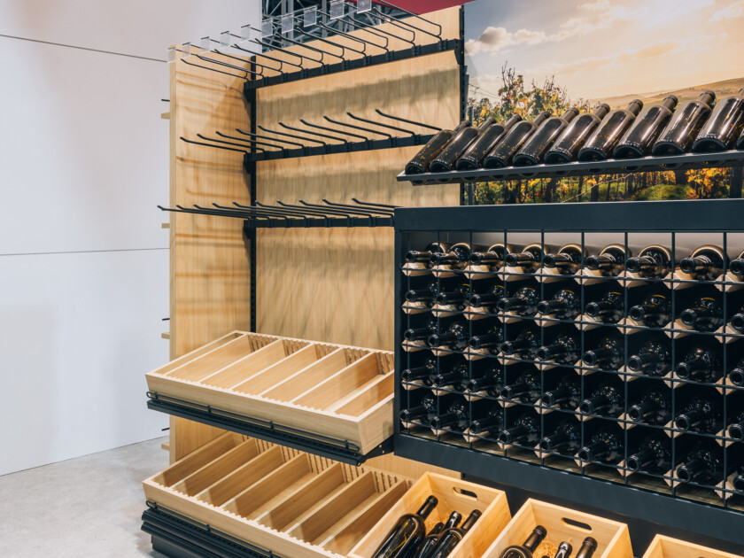 Gondola shelving display with wooden wine bottle holders and black metal wine rack, featuring adjustable shelves and product baskets at Euroshop 2023