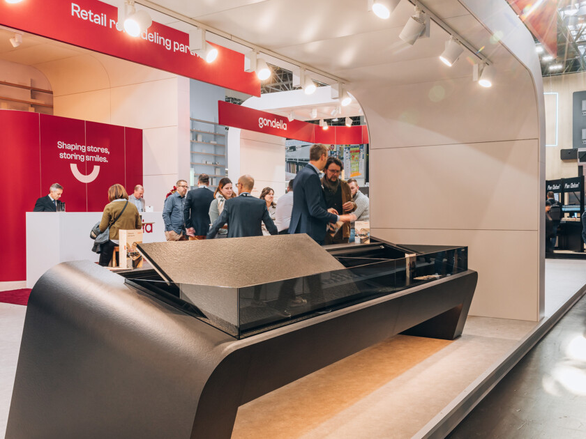 Gondella custom checkout counter with curved black design displayed at Euroshop 2023 trade show, visitors in background near red branded booth
