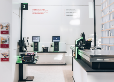 Self-checkout counters with SCO guidance systems, black baskets, and green accents in retail environment