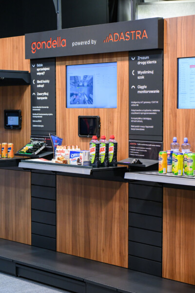 Gondella retail display booth at Warsaw trade show featuring Adastra IoT gateway integration, wooden shelving with product samples and beverages