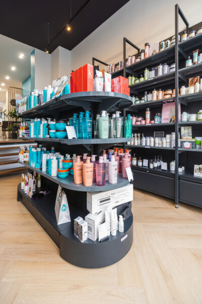 Circular black retail display with three tiers showing turquoise and pink hair care products, Pitch shelving with products in background