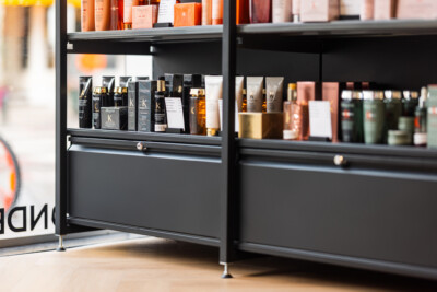 Black glass display cabinet with Kérastase hair care products, featuring shelving with orange and black packaging in a retail beauty setting
