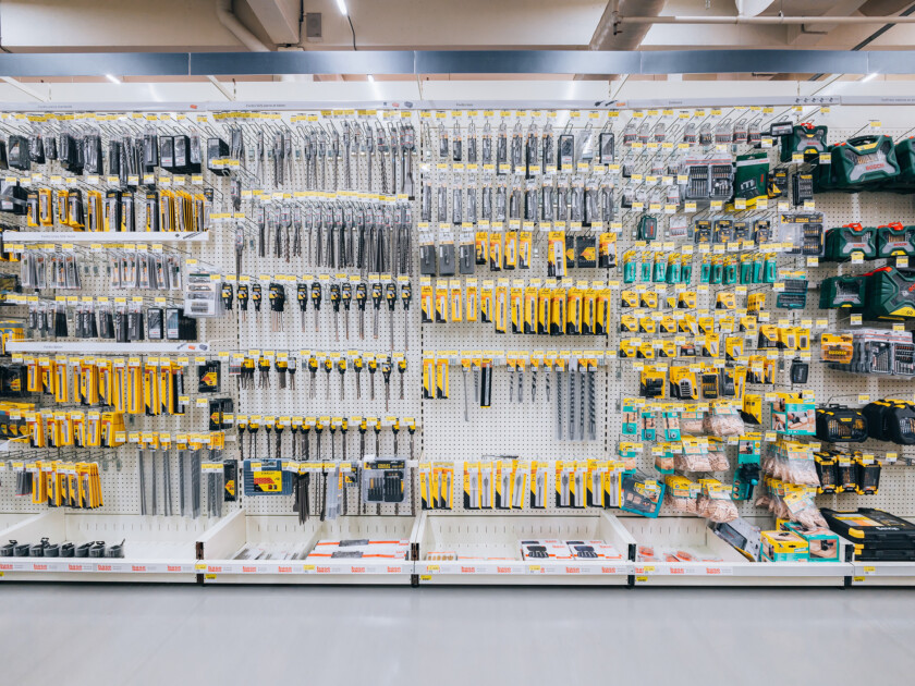 Pegboard wall display of power tools, drill bits, and hand tools in yellow packaging at a Brico retail store