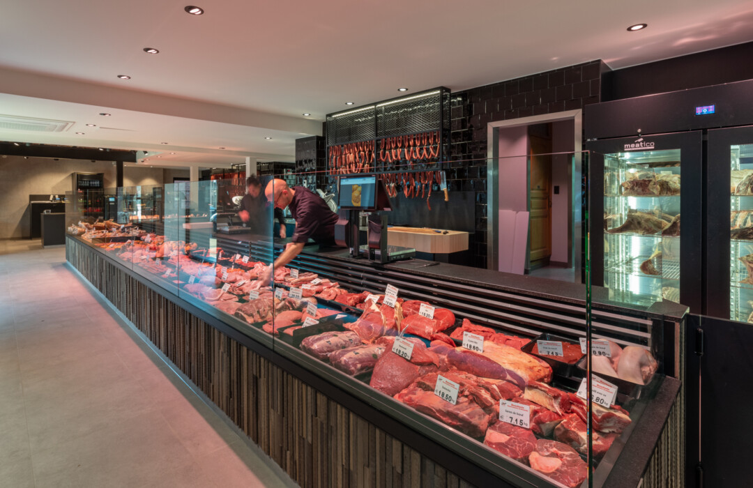 Butcher shop meat display counter with refrigerated glass case showing various cuts, cured meats, and sausages with price labels