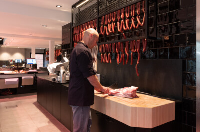 Butcher preparing cured sausages at specialty food retail counter with hanging products display