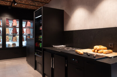 Bakery counter with black Gondola shelving displaying fresh bread, griddle cooktop, and refrigerated display case with pastries