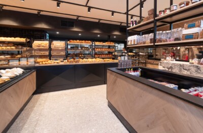 Modern bakery display with Gondola shelving units showcasing fresh bread and pastries, refrigerated counter with packaged goods, specialty food retail setup
