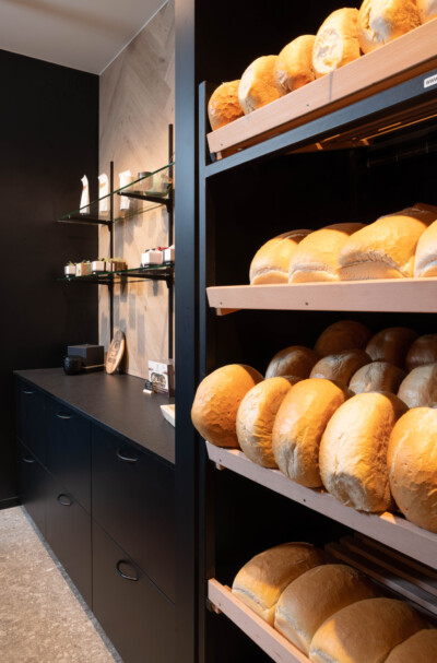 Pitch 41 shelving display with fresh bread and rolls in bakery retail setting, wooden shelves illuminated against dark background