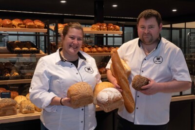 Bakery staff displaying artisan breads and pastries in front of wooden shelving display
