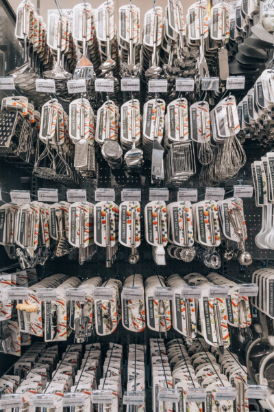 Retail kitchen utensils and cookware display with packaged cutlery sets and cooking tools on black pegboard shelving