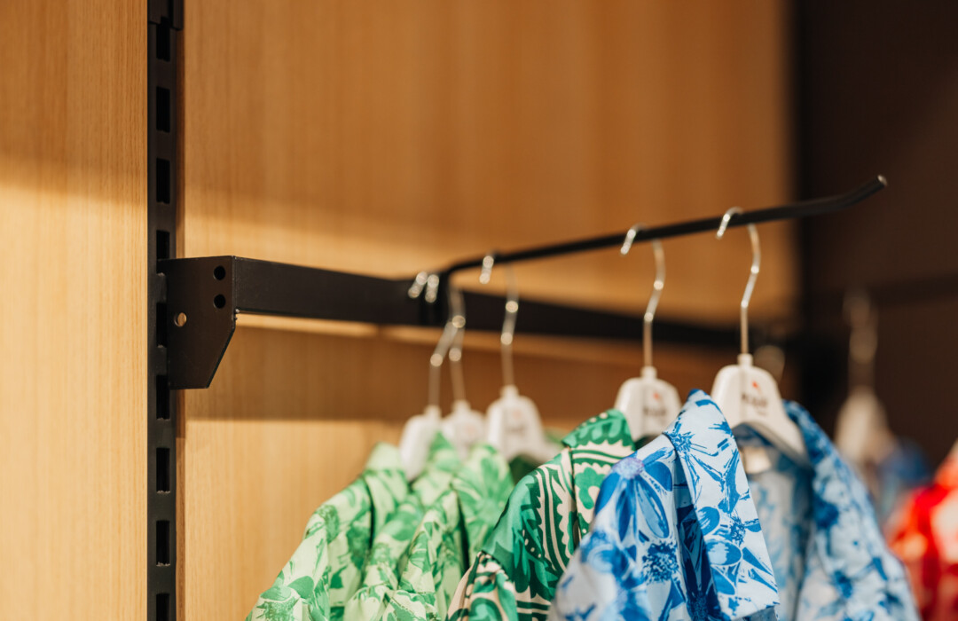 Blue and green patterned garments on white hangers hanging from black retail rod mounted on wooden wall
