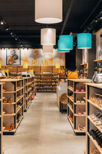 Children's fashion retail store with Pitch shelving displaying footwear, turquoise pendant lighting, wooden display units
