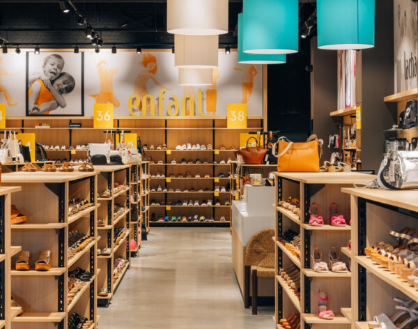 Children's fashion retail store with Pitch shelving displaying footwear, turquoise pendant lighting, wooden display units