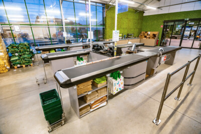 Supermarket checkout area with Gondella counters, conveyor belt checkouts, and cardboard display units on polished concrete floor