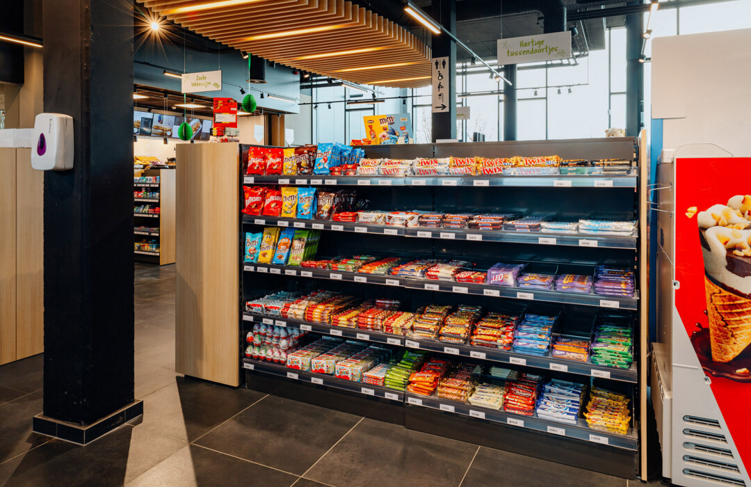 Pitch 25 shelving displaying confectionery and snacks in Delhaize supermarket with illuminated wooden ceiling