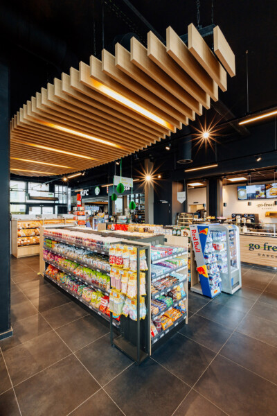 Modern convenience store with wooden slatted ceiling, central product displays, KFC counter, go-fresh bakery, and refrigerated beverage cooler
