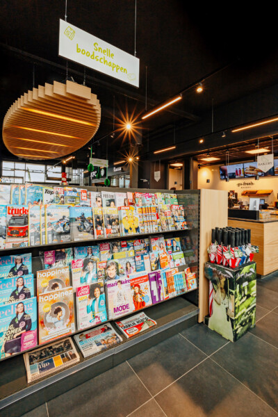 Service station retail display with magazine shelving, Pitch 25 gondola unit with illuminated wooden header, checkout counter visible