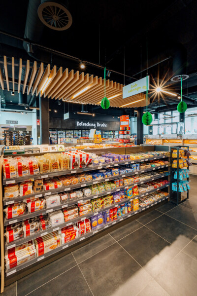 Pitch 25 shelving display with packaged snacks and confectionery in modern supermarket interior with illuminated wooden ceiling