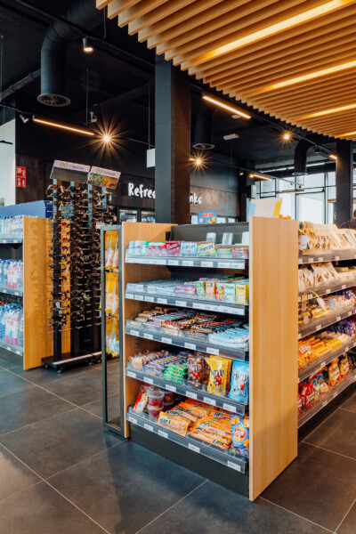 REWE convenience store with Pitch 25 shelving displaying snacks, beverages and confectionery with wooden end-cap display
