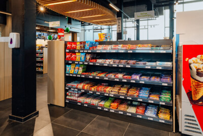 Pitch 25 shelving displaying confectionery and snacks in Delhaize supermarket with illuminated wooden ceiling