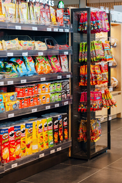 Pitch 25 shelving displaying snacks and beverages in Delhaize supermarket with pegboard fixture for hanging products