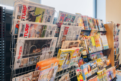 Magazine and newspaper display rack with multiple shelves holding publications and retail media