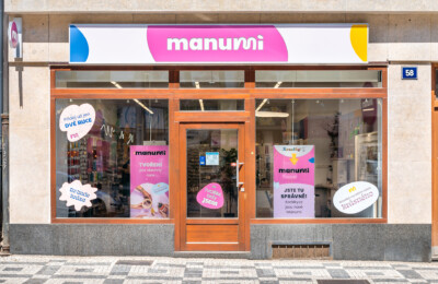 Manumi retail storefront with orange framing, pink signage, and display windows showing beauty and craft products