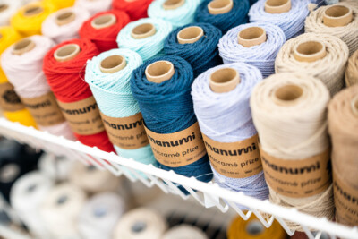 Colorful macramé thread spools in various colors including blue, white, red, and cream with kraft paper labels