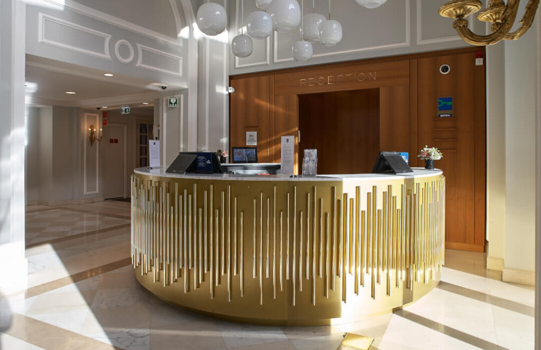 Hotel reception desk with gold fluted front panel, marble flooring, and wooden feature wall