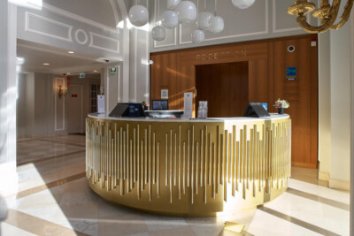 Hotel reception desk with gold fluted front panel, marble flooring, and wooden feature wall