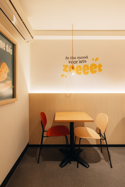 Panos Lokeren break room with wooden table, chairs, and yellow 'In the mood voor iets zwaeet' wall text