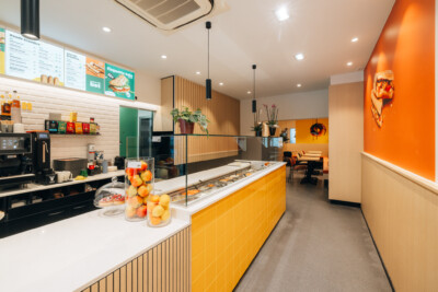 Modern fast-food counter with yellow tile cladding, white countertop, product display case, and orange accent wall in quick-service restaurant